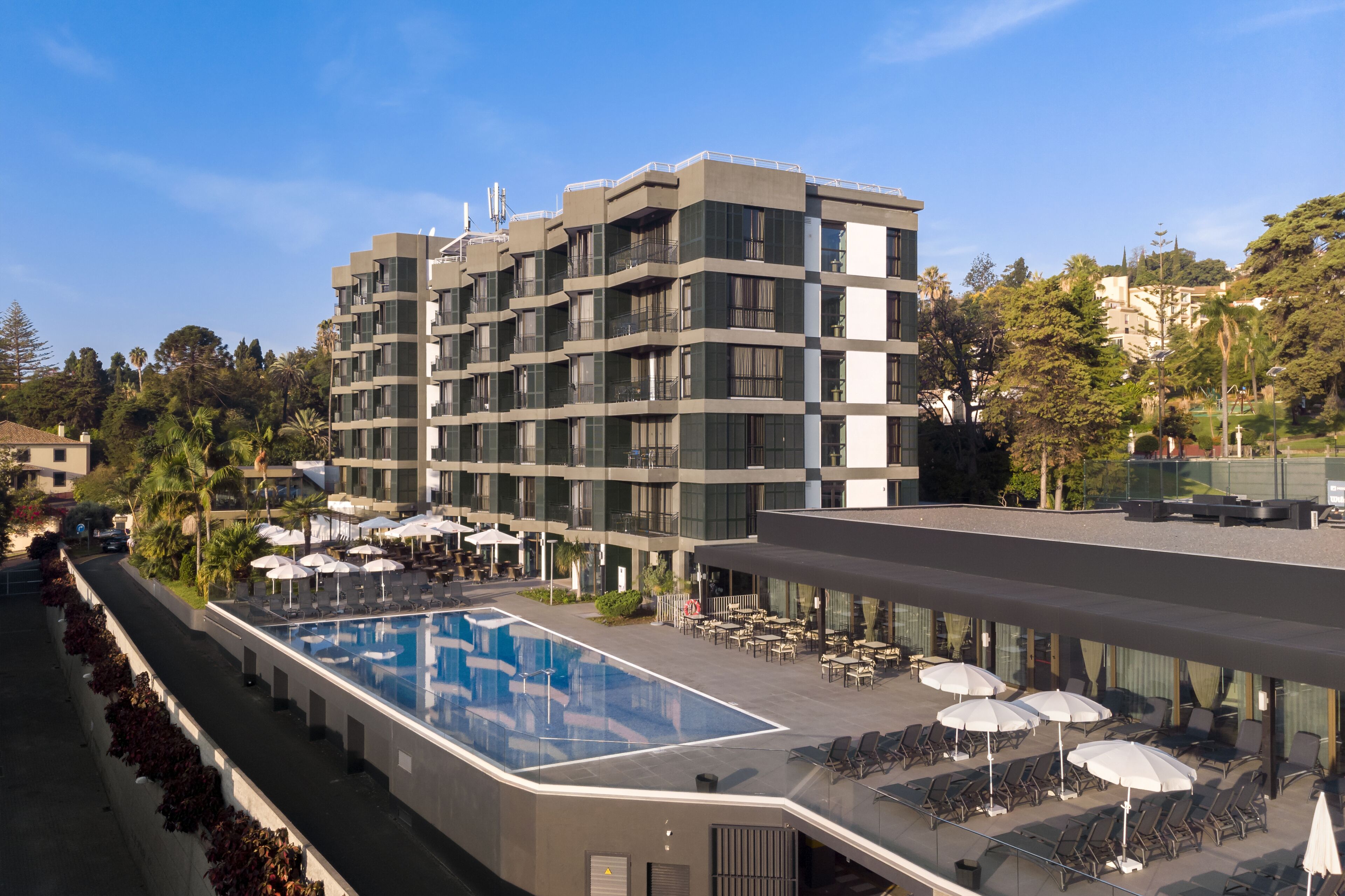 Un hôtel moderne doté d’une piscine sur le toit, d’un espace extérieur aménagé et offrant une vue sur les bâtiments et les arbres environnants.