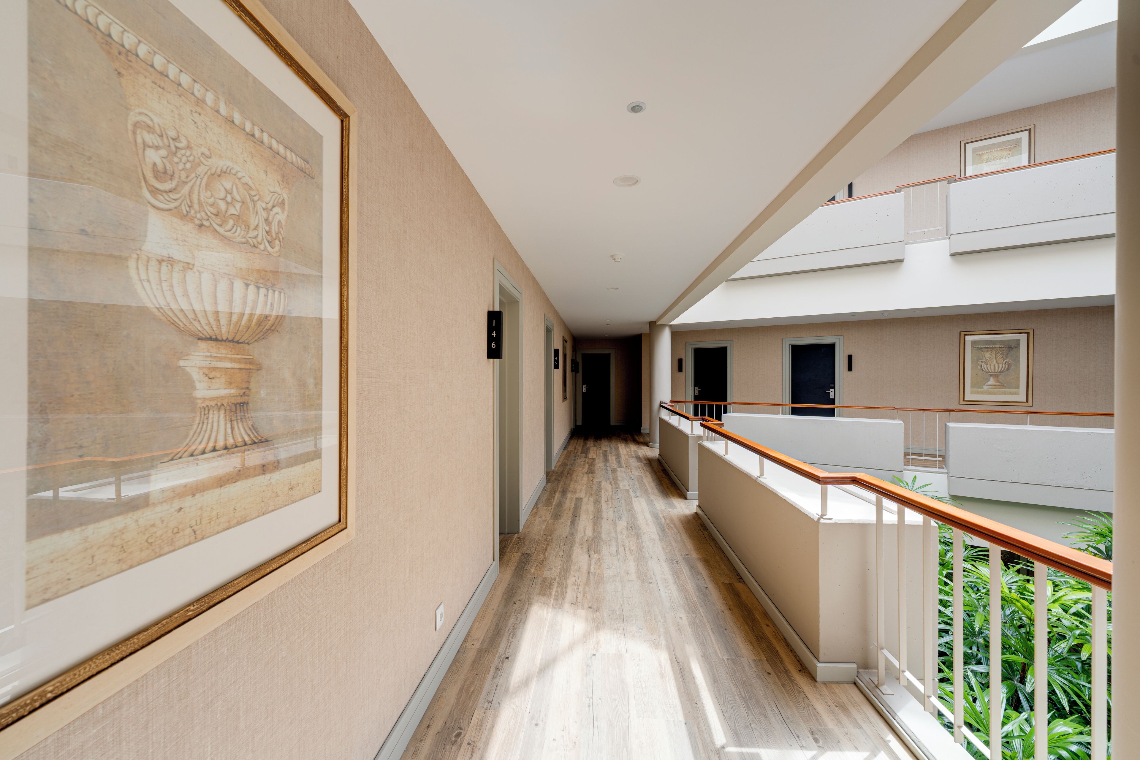 A hotel corridor with a wooden floor, a framed artwork on the wall, and a balcony with a railing.