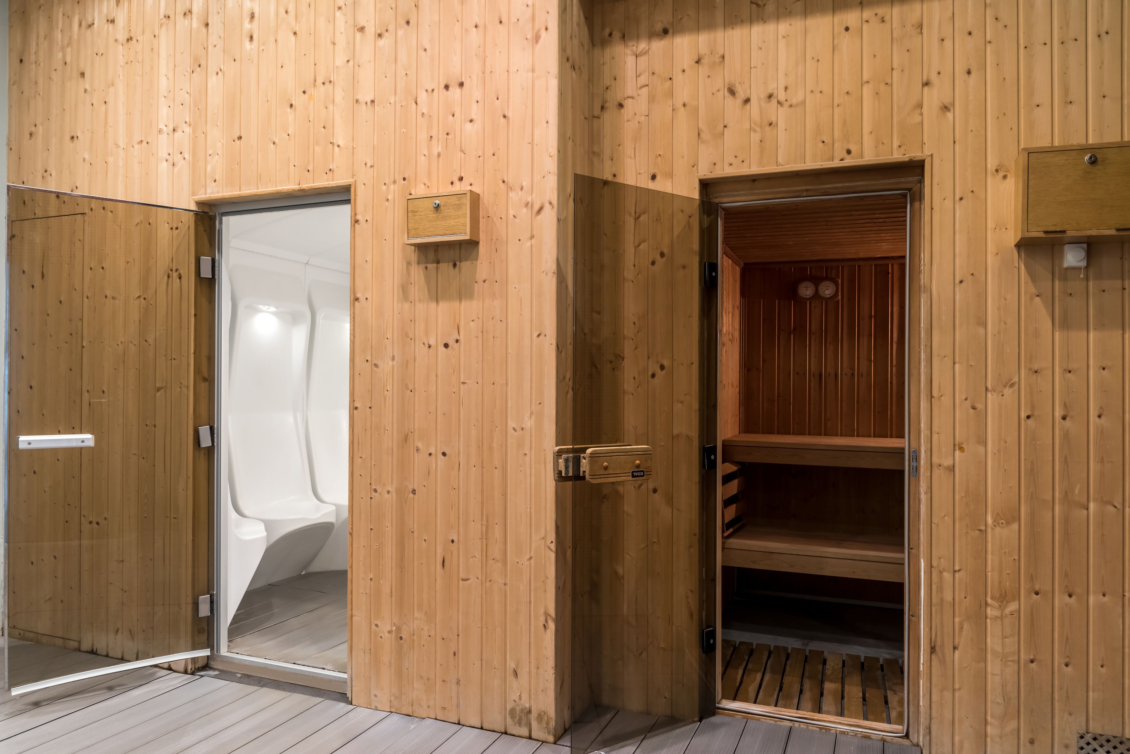 A wooden interior with a glass door leading to a toilet, a wooden door with a handle, and a shelf unit with a wooden slatted design.