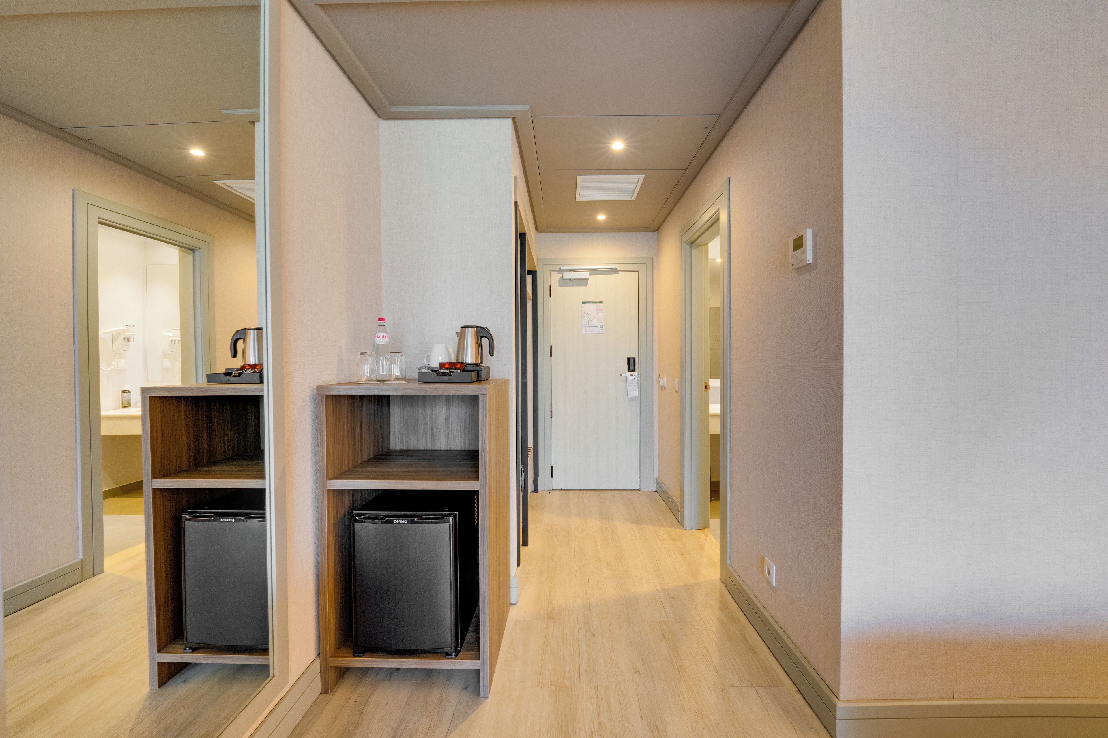 Ein Hotelgang mit Holzboden, einer Küchenzeile inklusive Kaffeemaschine und Kühlschrank, sowie einer Tür mit Thermostat.
