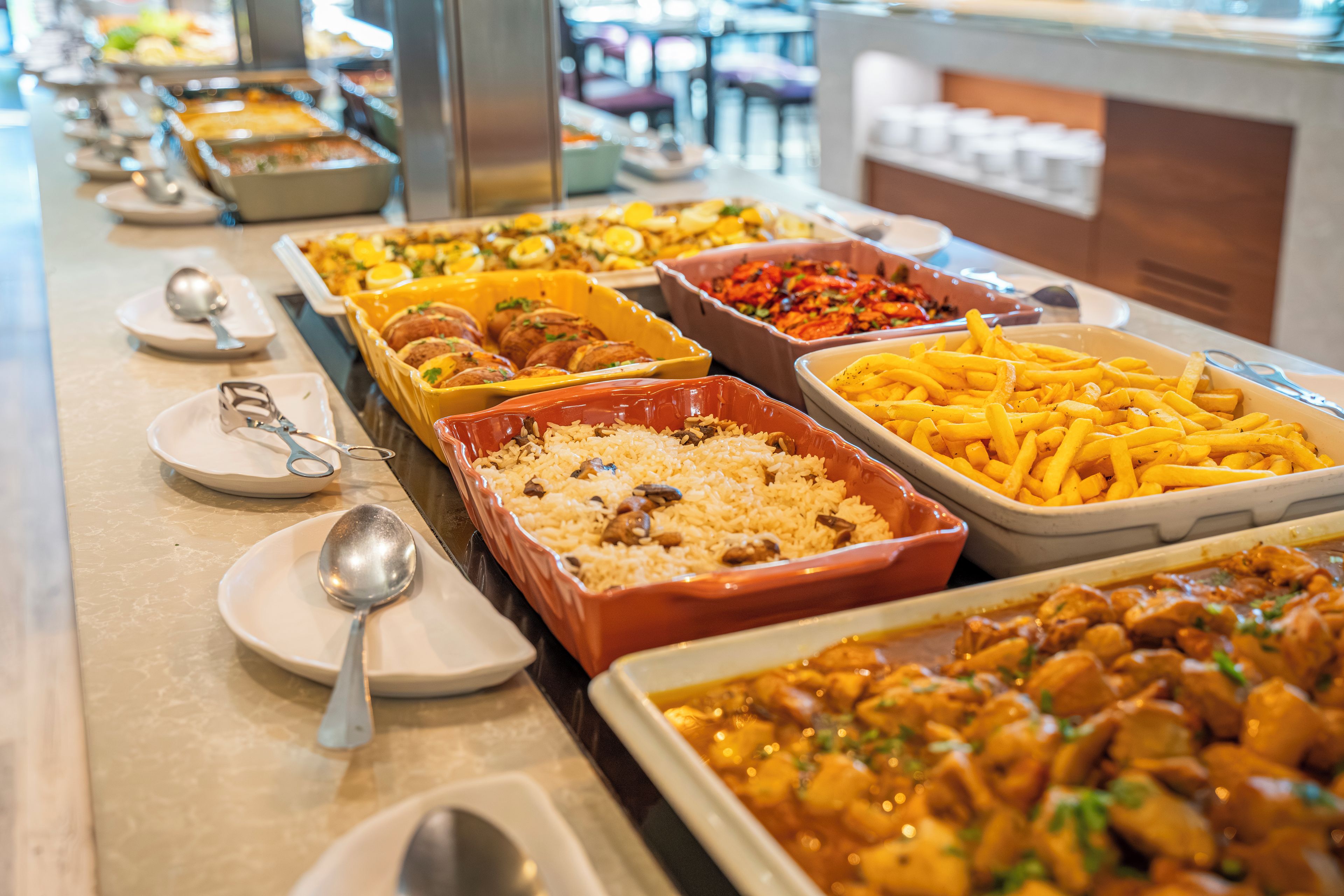 A buffet table with various dishes including rice, meat, and French fries.