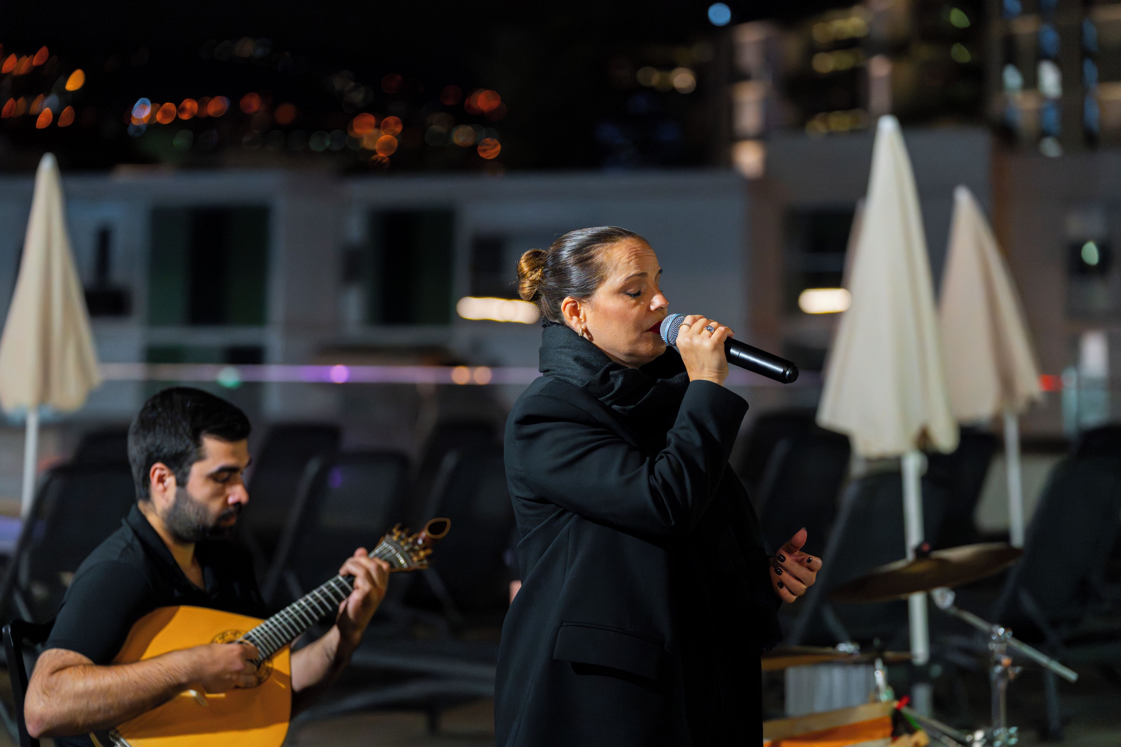 A person singing into a microphone with a guitar player in the background.