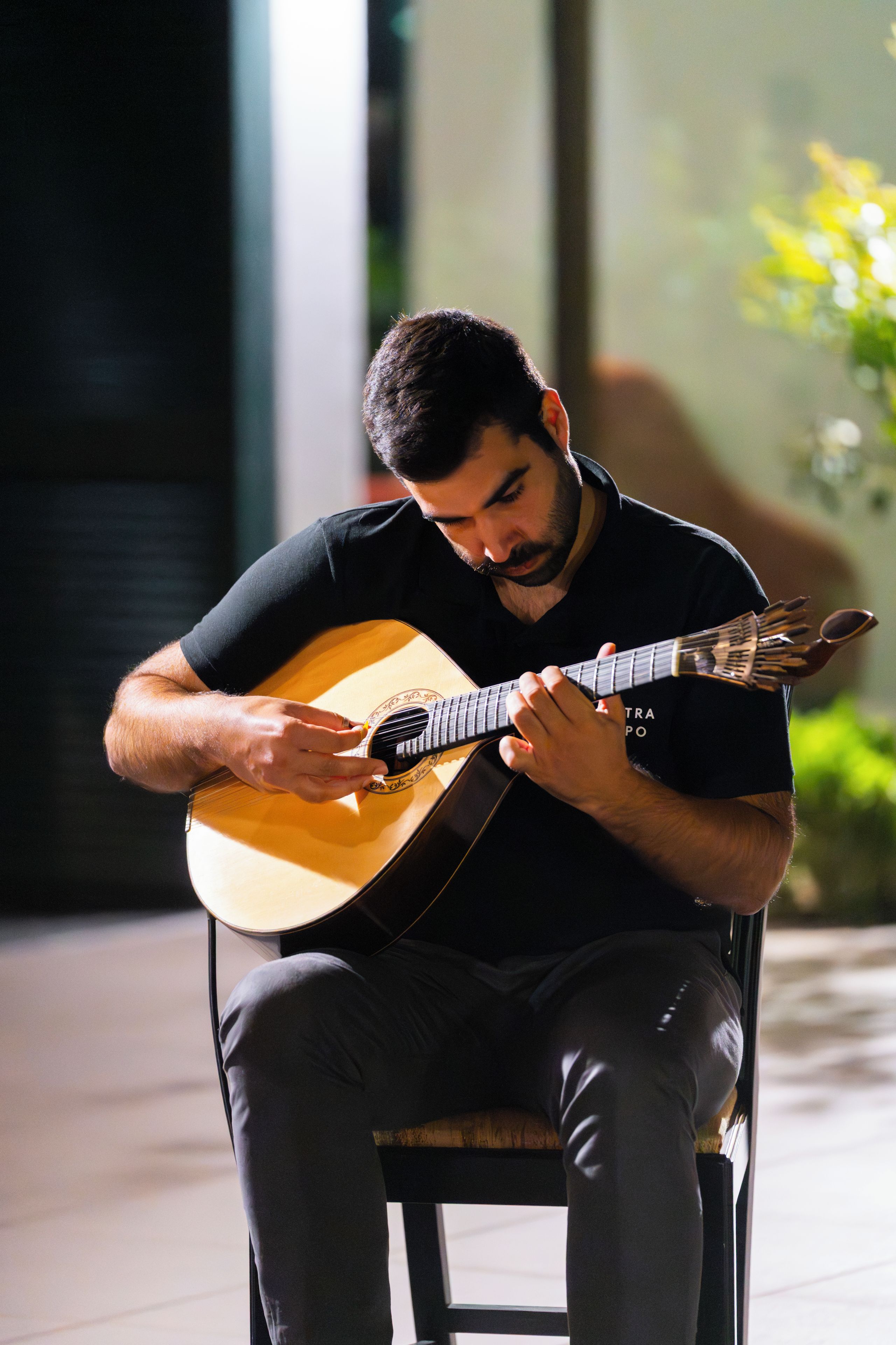 A person seated on a chair playing a guitar.