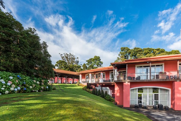 A hotel with a red facade, a covered outdoor seating area, and a well-maintained garden with hydrangeas.