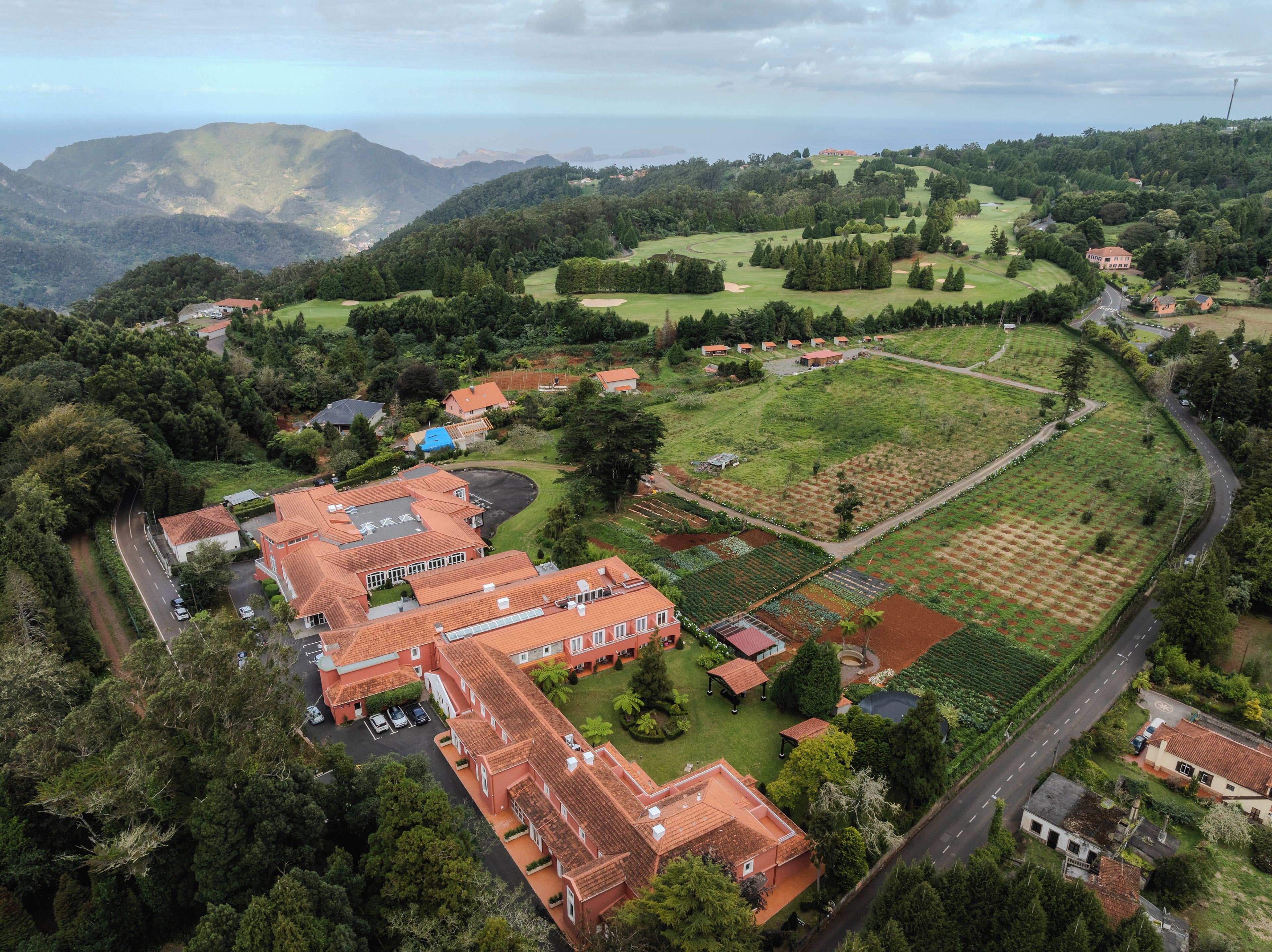 A residential area with a large building featuring a red-tiled roof, surrounded by lush greenery and a golf course.