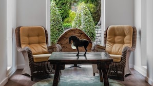 A room with two wicker chairs, a wooden table, and a view of a lush garden through a large window. - Enotel Santo da Serra (Machico)