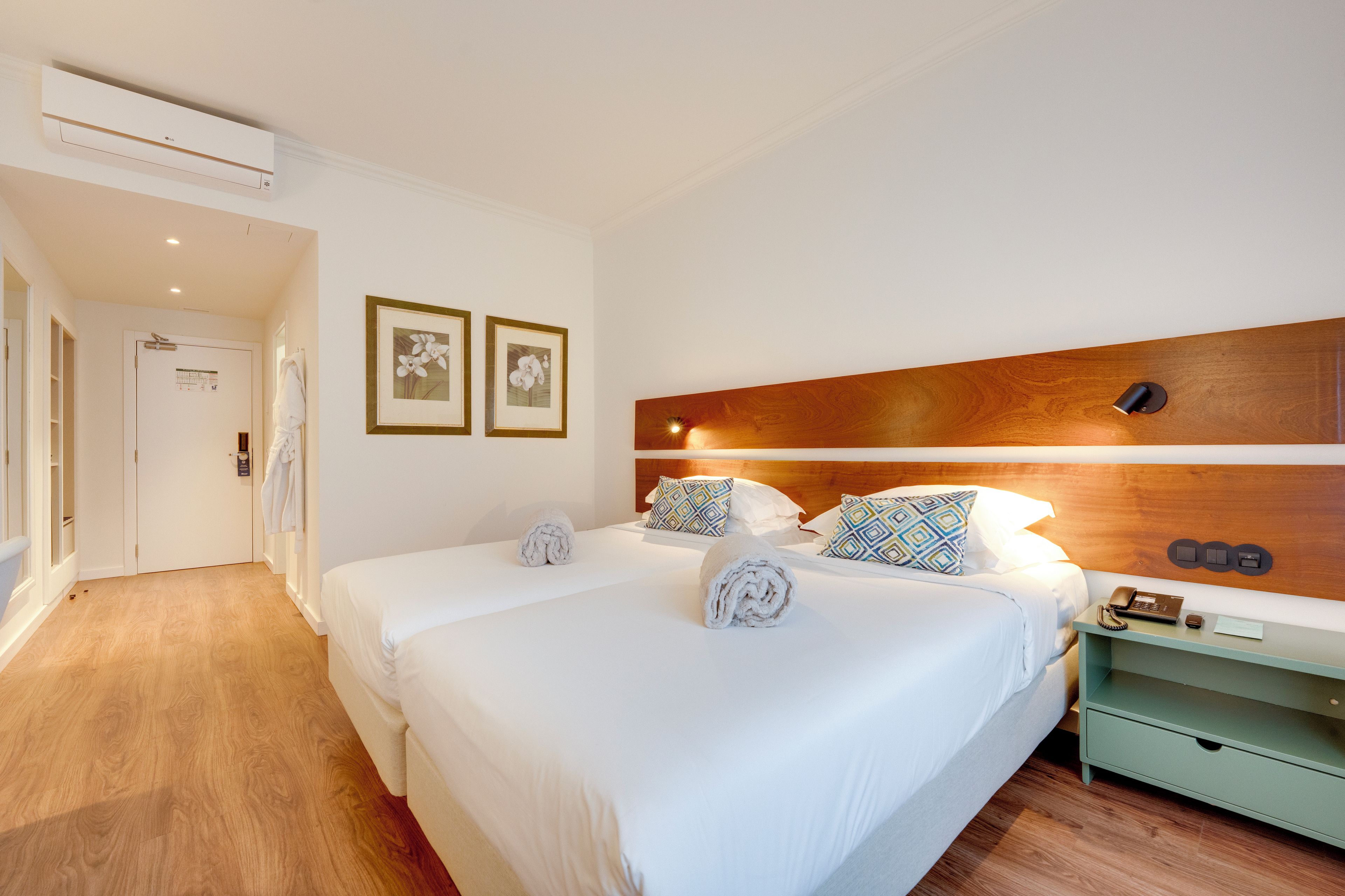 A hotel room with a double bed, a nightstand, a wooden headboard, and two framed pictures on the wall.