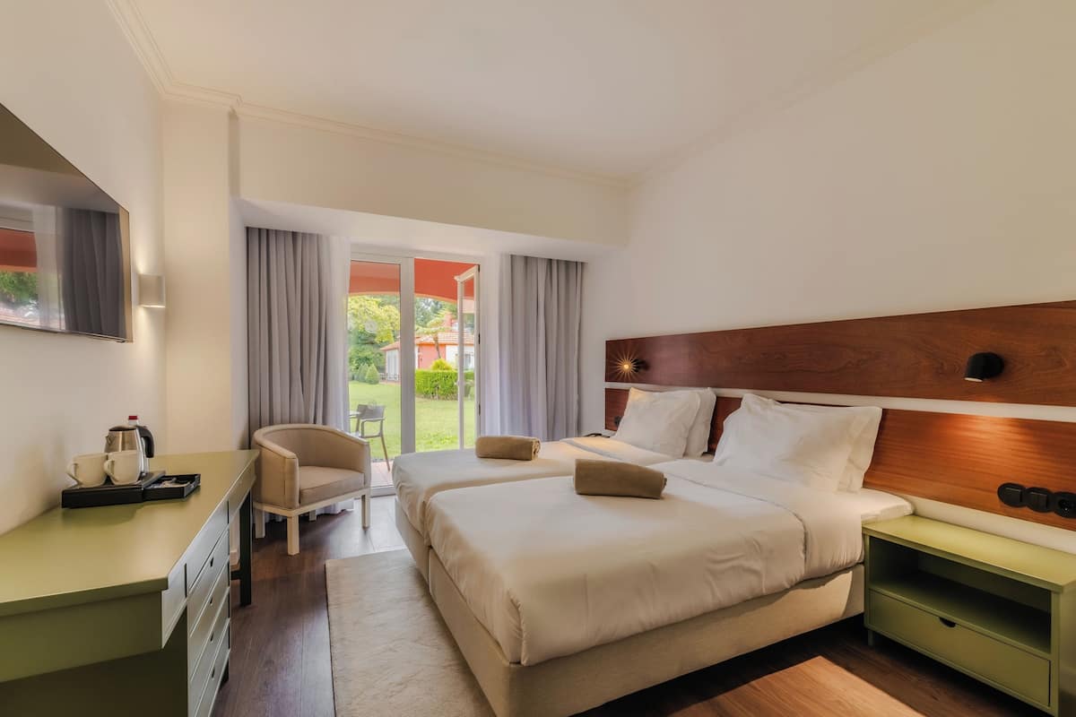 A hotel room with two beds, a desk, a chair, and a view of the outdoors.