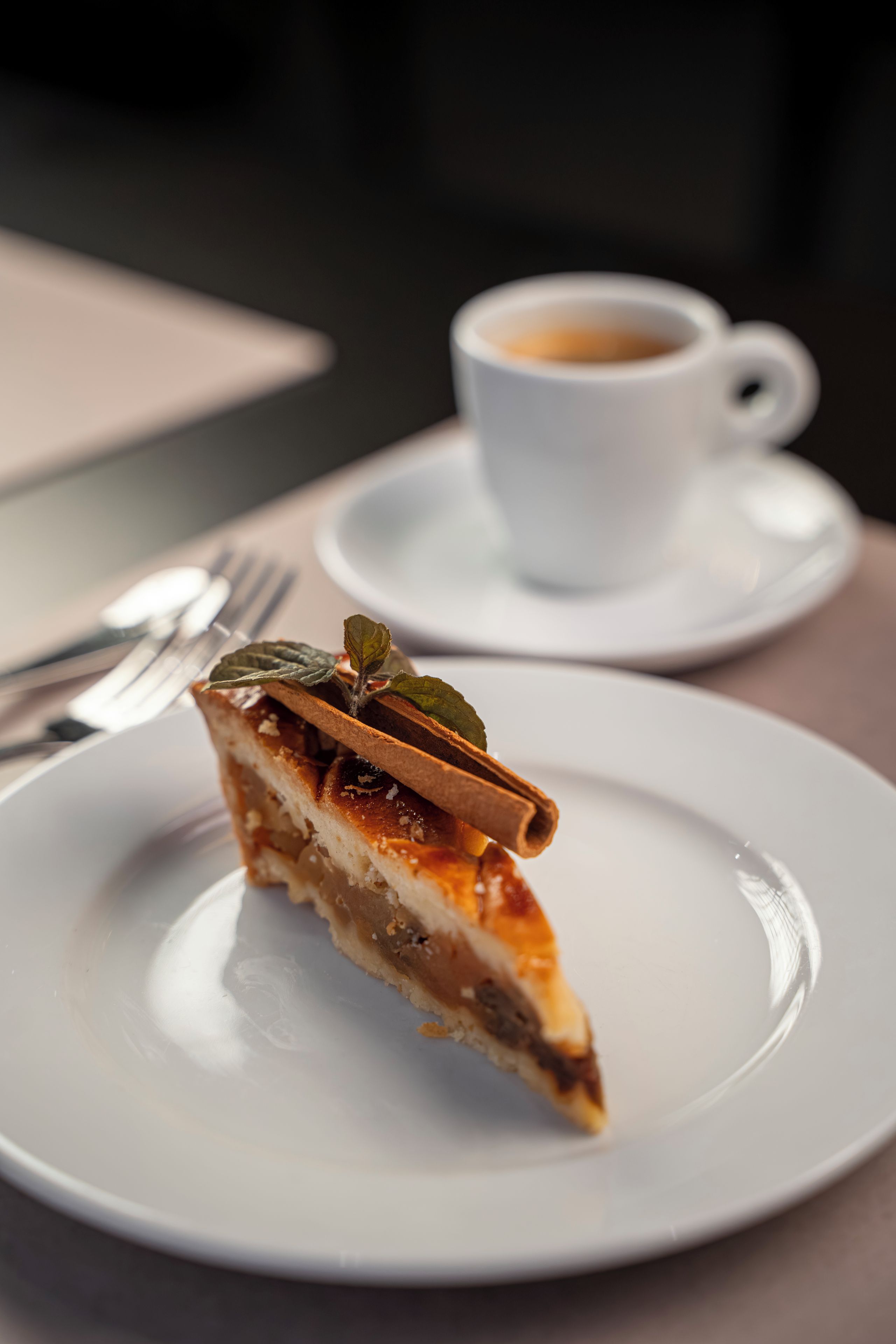 A slice of cake on a plate with a cup of coffee in the background.