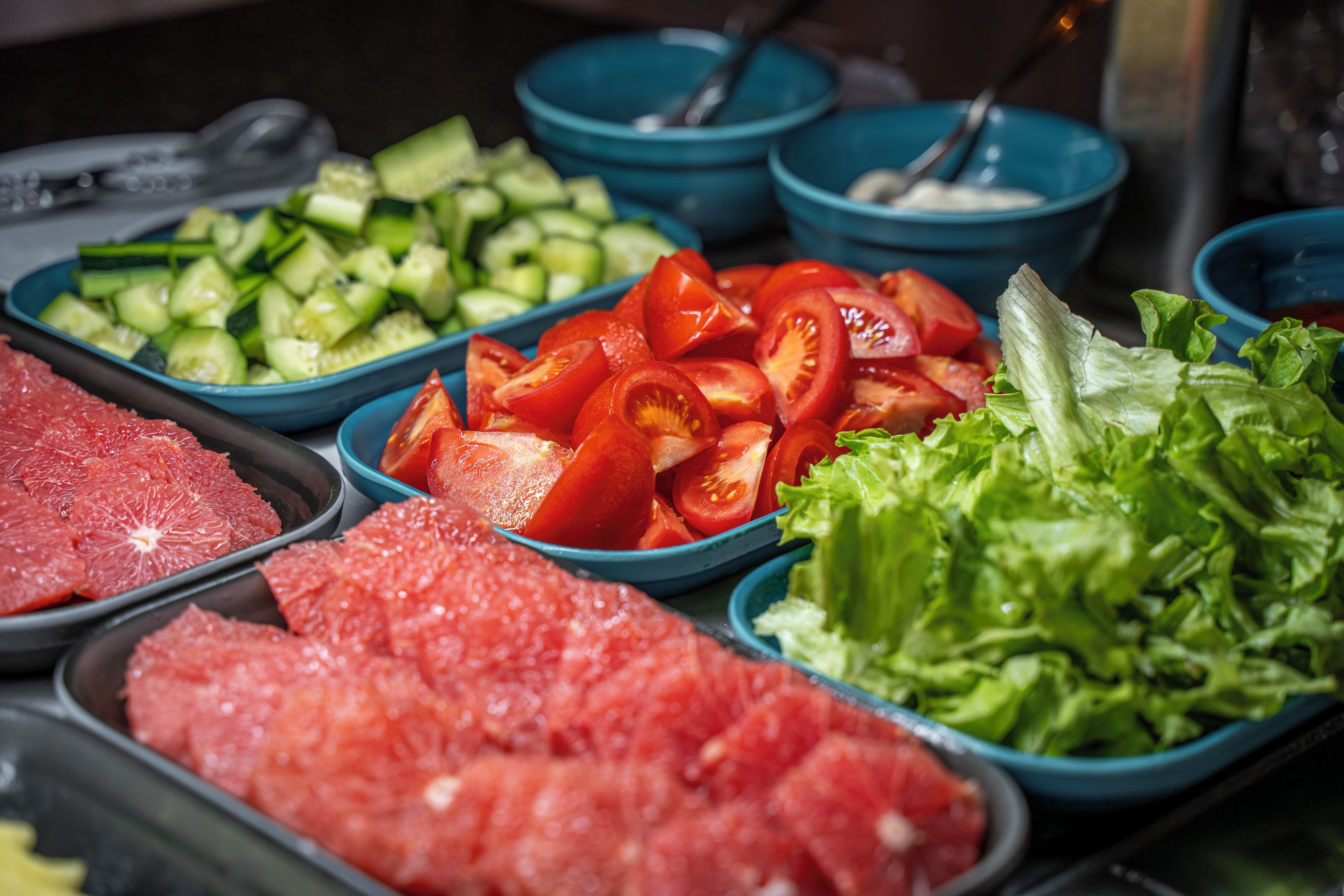 A buffet with various food items including sliced tomatoes, cucumbers, lettuce, and meat.