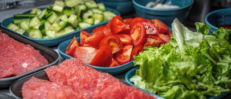 A buffet with various food items including sliced tomatoes, cucumbers, lettuce, and meat.