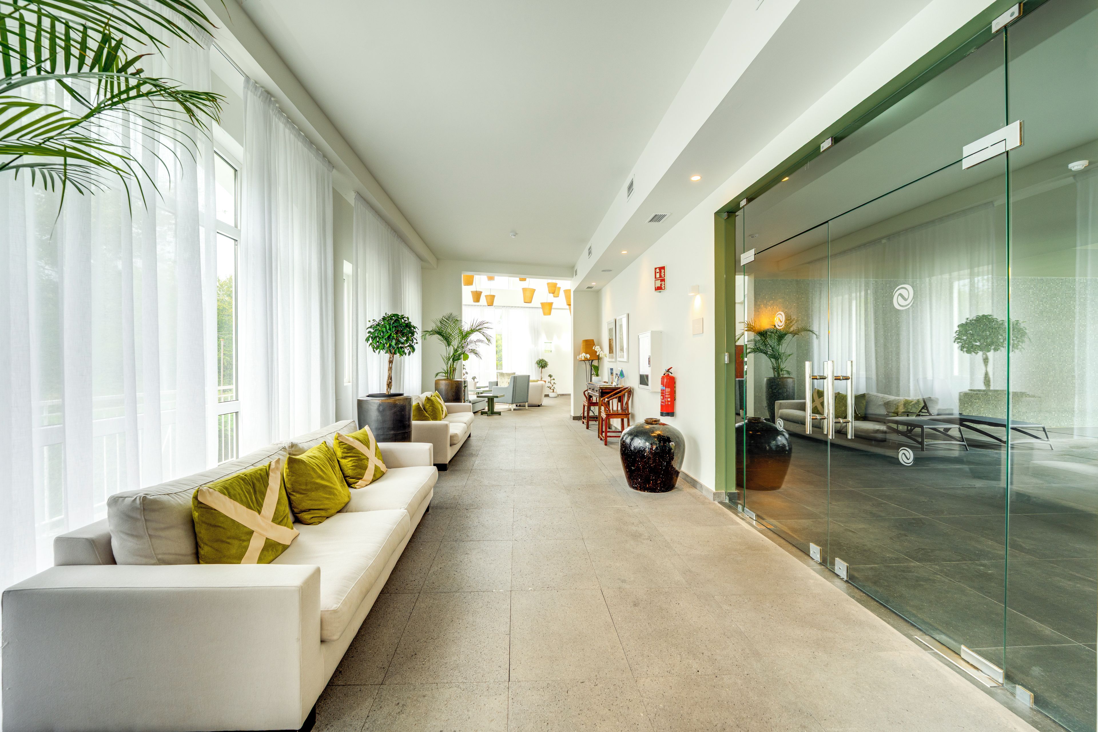 A hotel lobby with a long reception desk, seating area with sofas, and a glass wall.