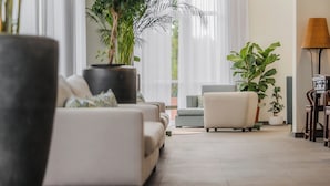 A modern living room with a sofa, a coffee table, and a large potted plant. There are hanging lights and a window with curtains. - Enotel Santo da Serra (Machico)