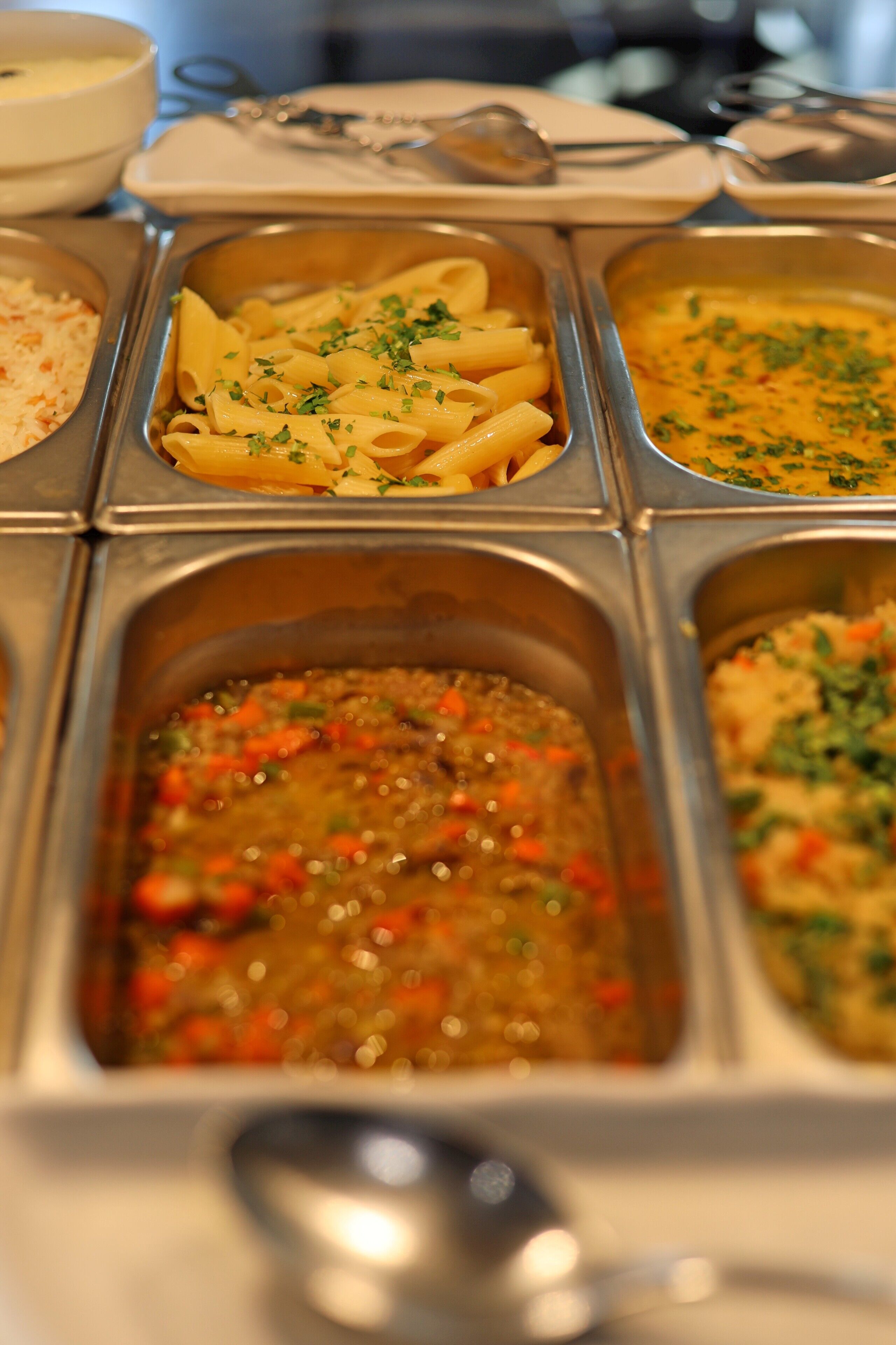 A buffet with various dishes including pasta, a creamy soup, and a vegetable stew.