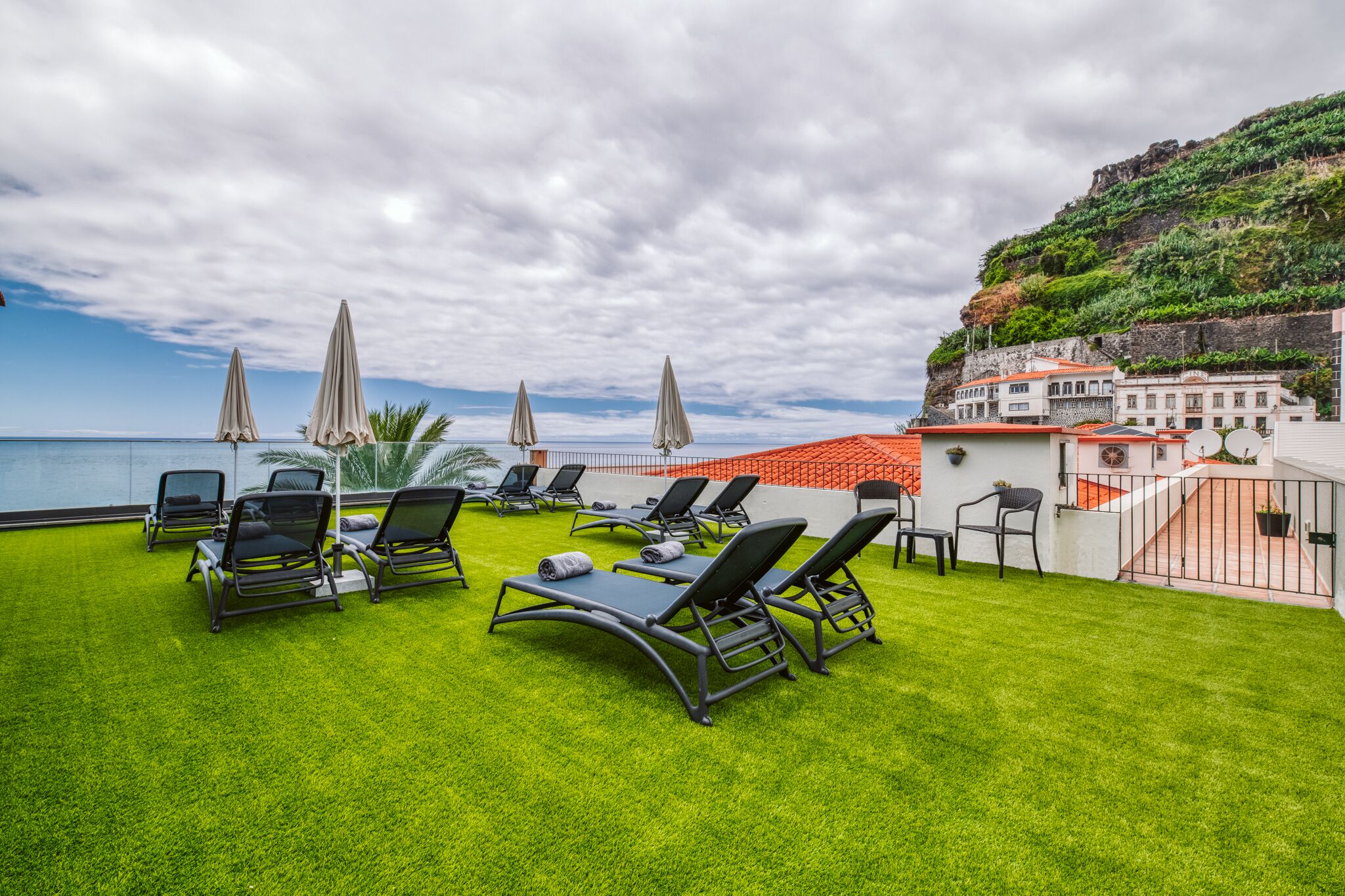 A rooftop terrace with sun loungers and umbrellas overlooking a coastal area.