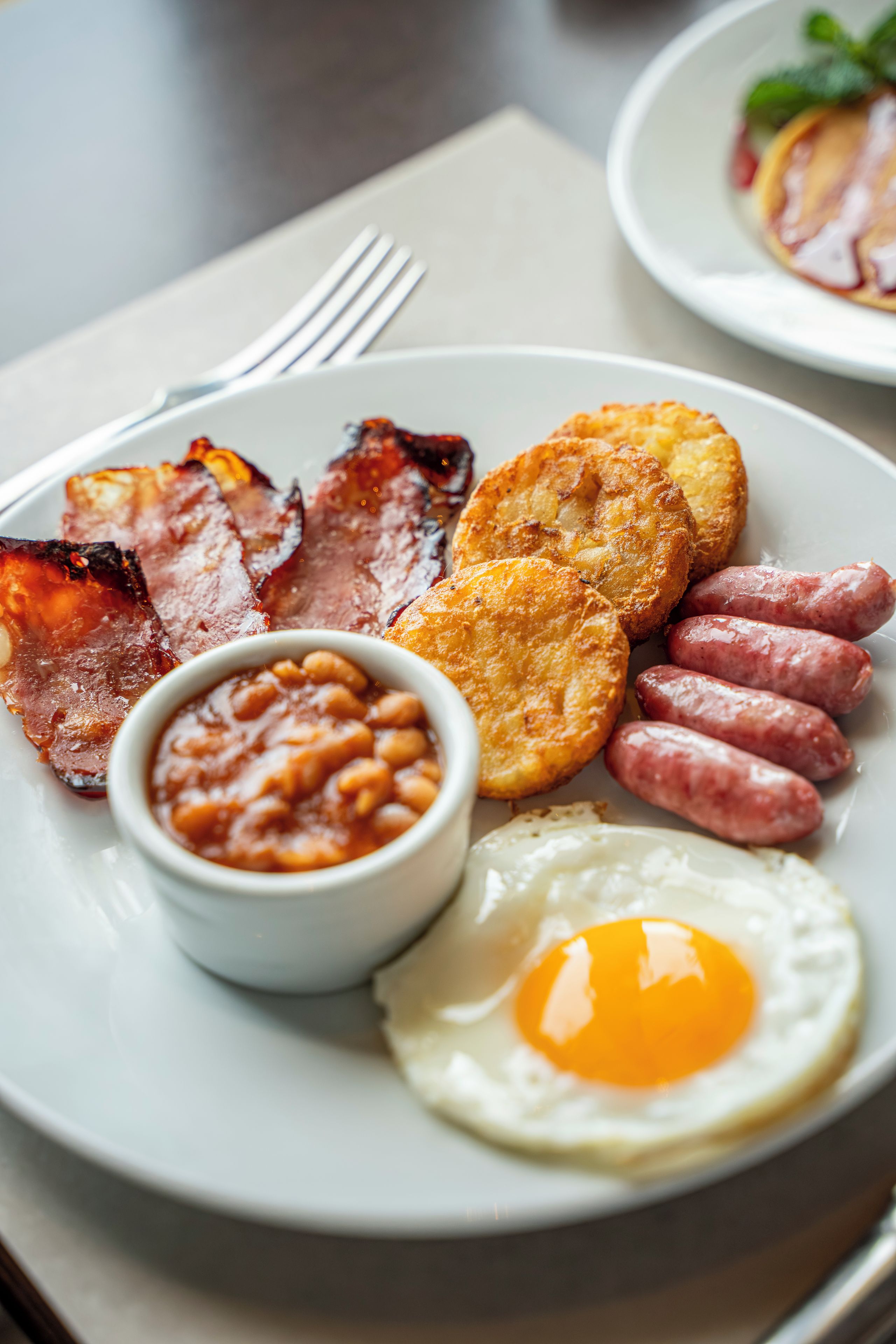 A plate of breakfast food including bacon, sausages, fried eggs, and beans.