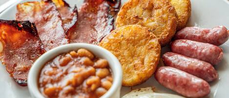 A plate of breakfast food including bacon, sausages, fried eggs, and beans.
