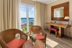 A hotel room with a balcony, wicker chairs, a small table, a wooden desk, and a mirror. - Enotel Sunset Bay (Ponta do Sol)