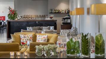 A modern hotel lobby with a sofa set, decorative vases, and a bar area with cocktail bottles.