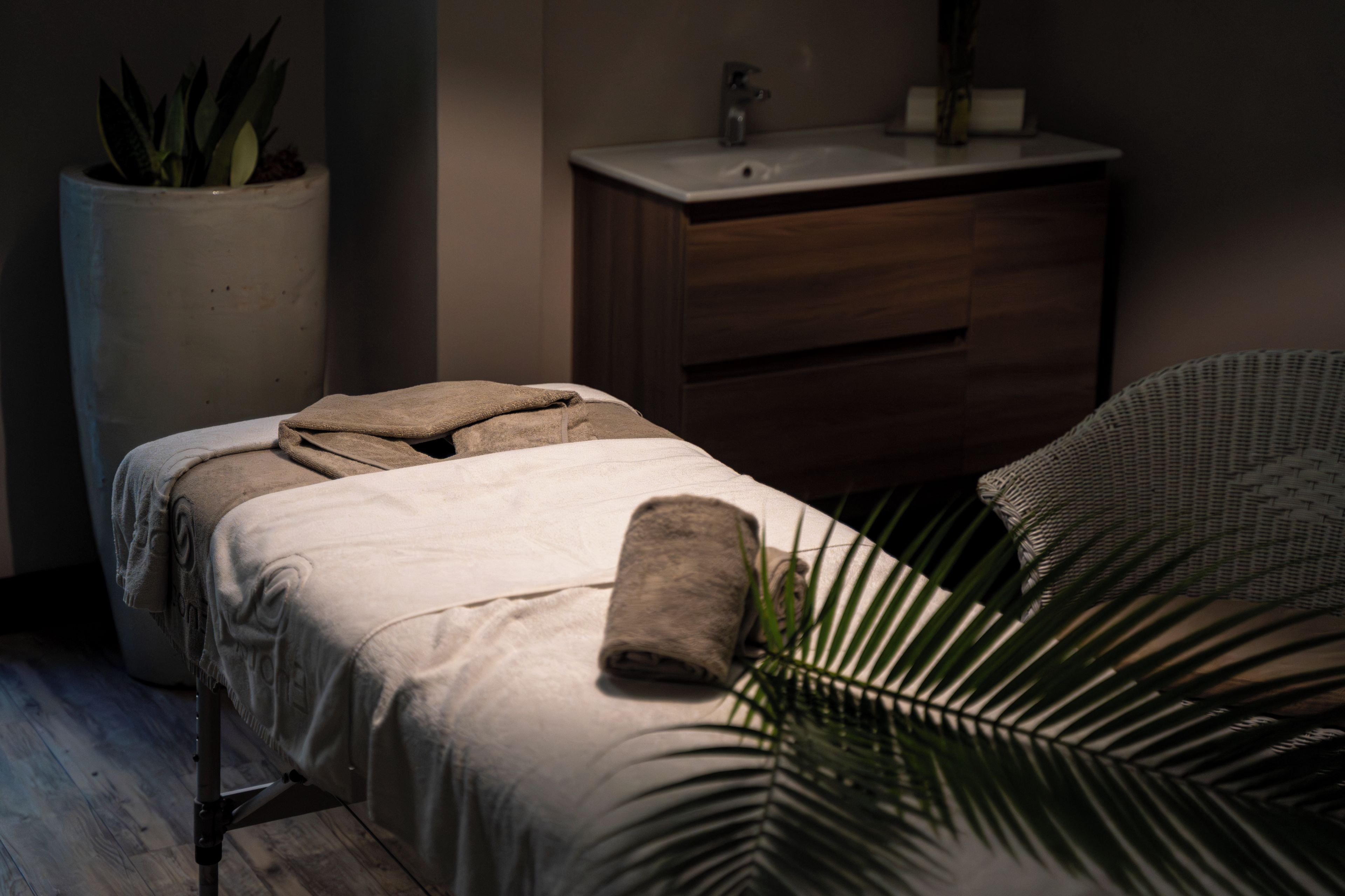 Una sala de spa con una cama, una toalla, un lavamanos y una planta en maceta.