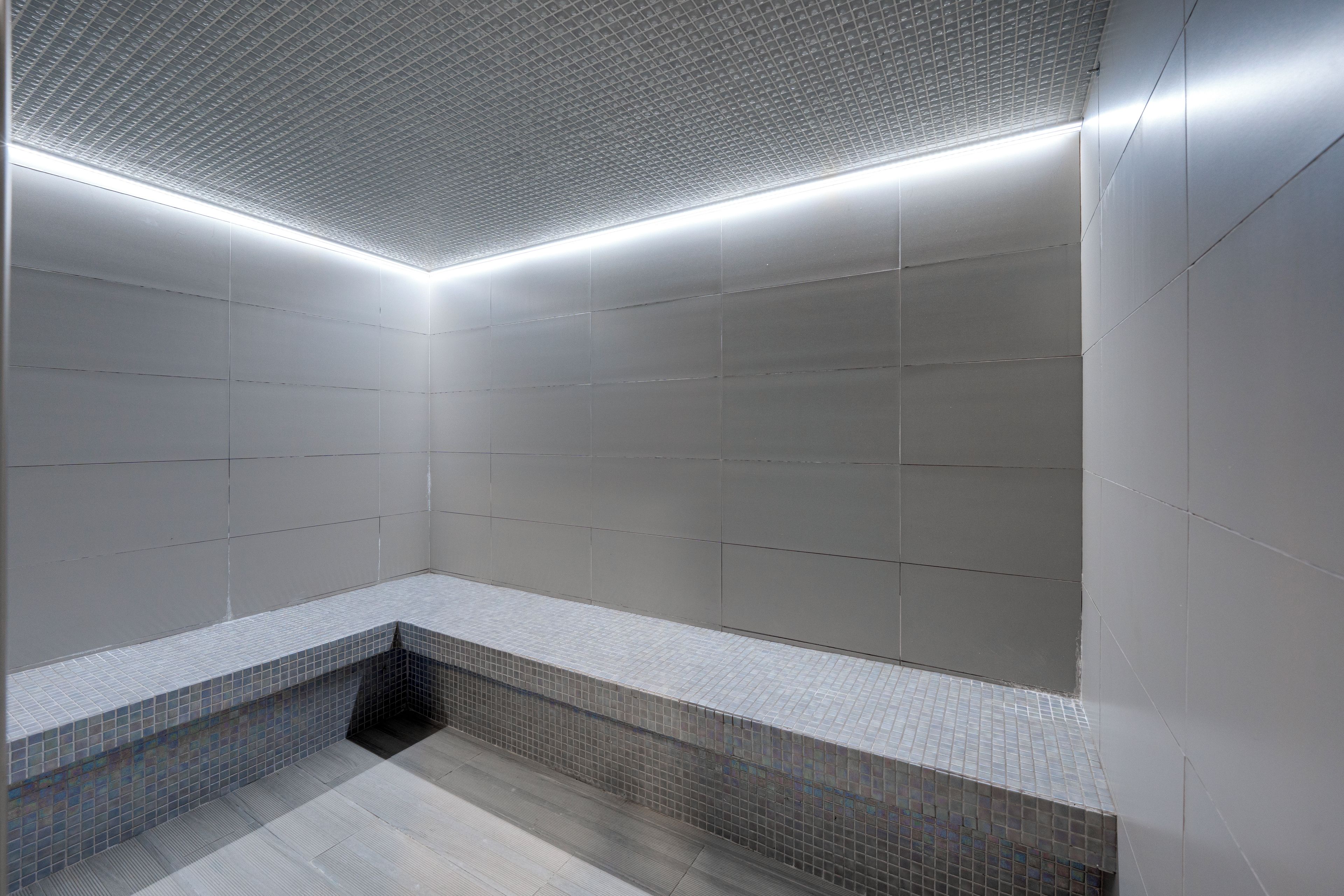 A modern bathroom with a tiled floor, a bench, and a ceiling with a grid pattern.