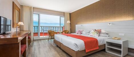 A hotel room with a bed, a desk, a chair, a nightstand, and a large window with a balcony.