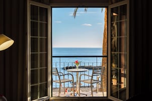Vista desde una habitación con balcón que da a una playa, con una mesa, sillas y un jarrón de flores.