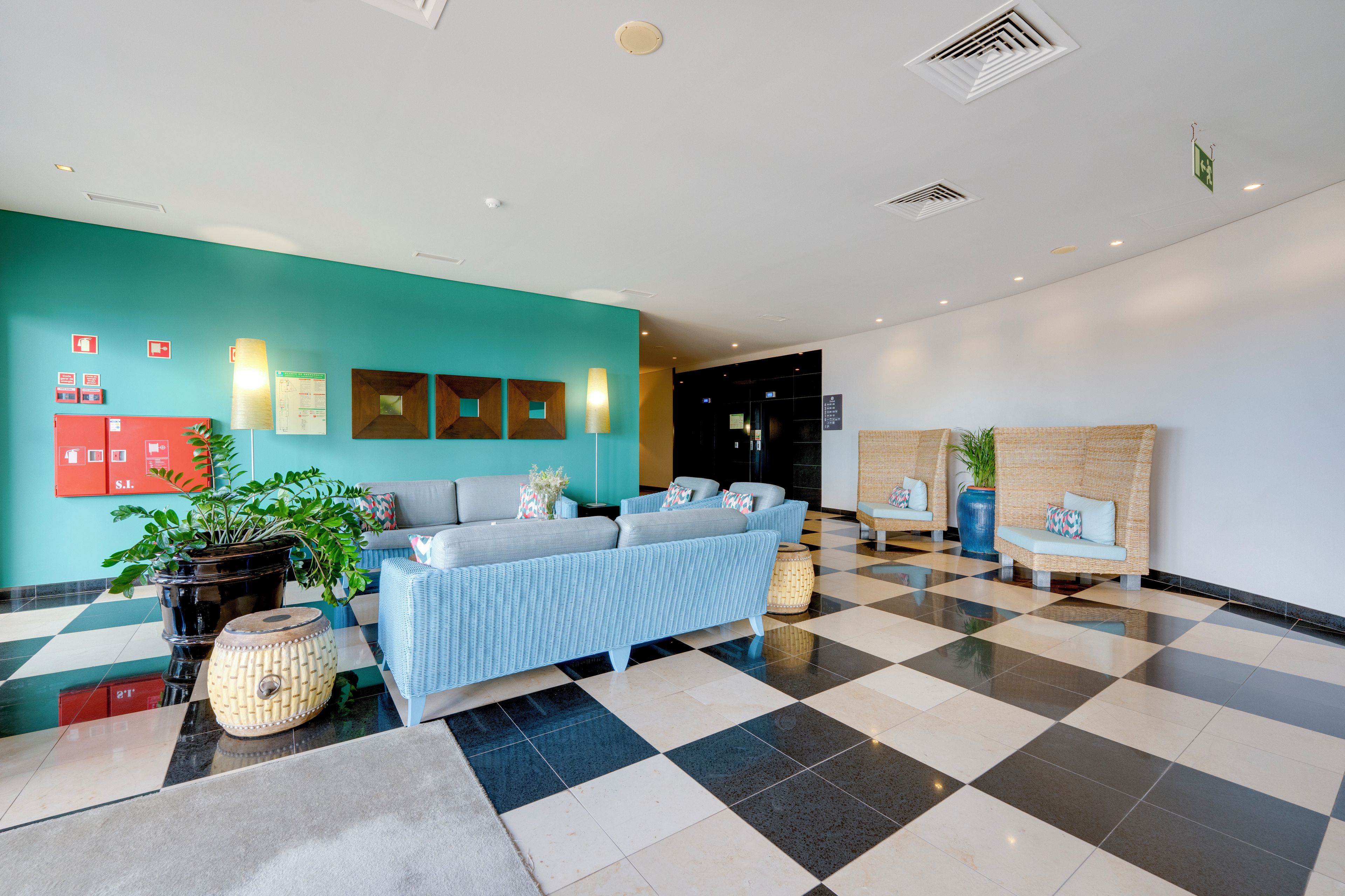 A lobby with a checkered floor, a sofa, a plant, and a wall with emergency exit signs.