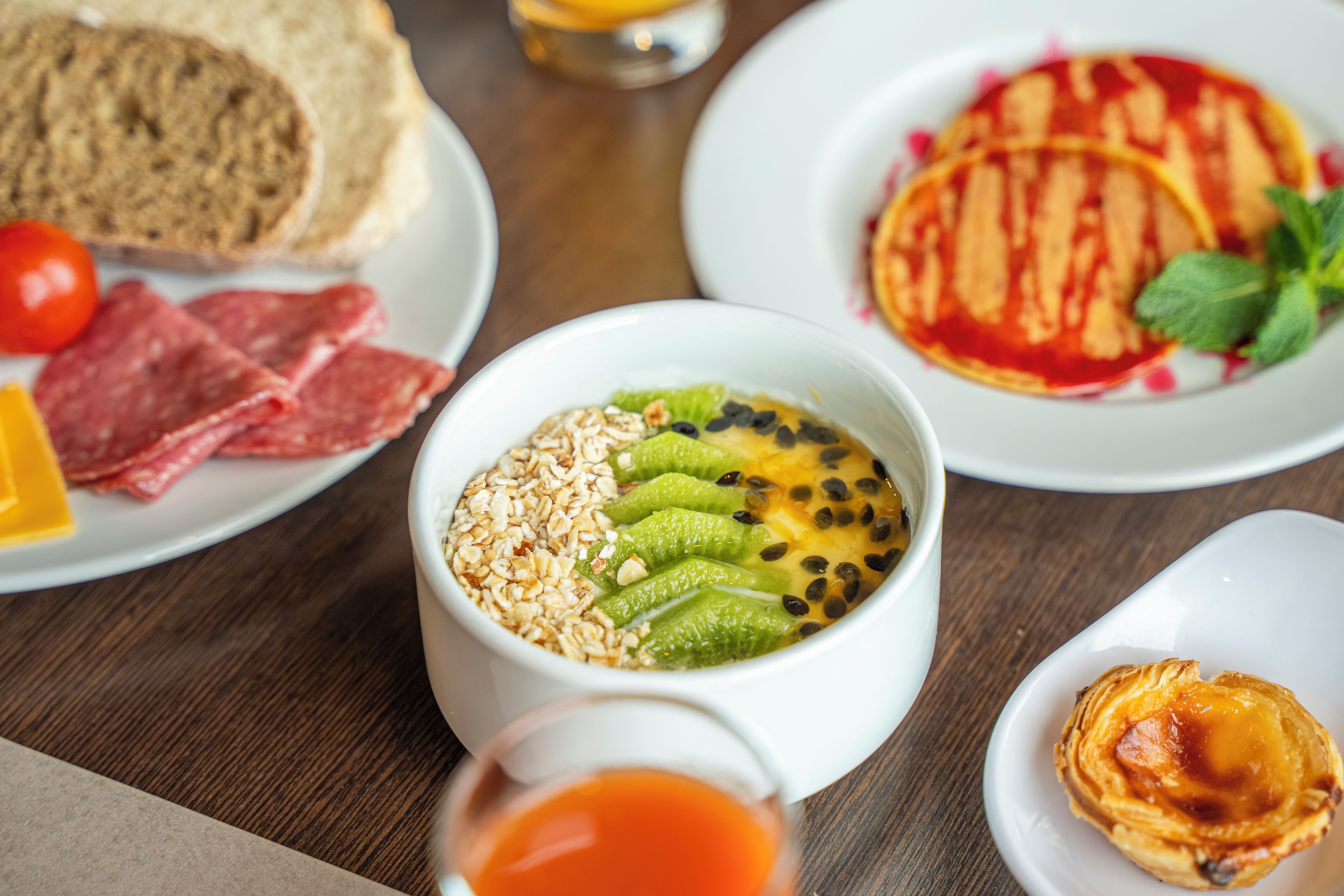 A variety of food items on plates, including toast, a slice of pizza, and a bowl with avocado and seeds.