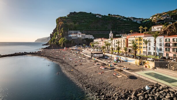 Un pueblo costero con una playa rocosa, edificios con balcones e iglesia.