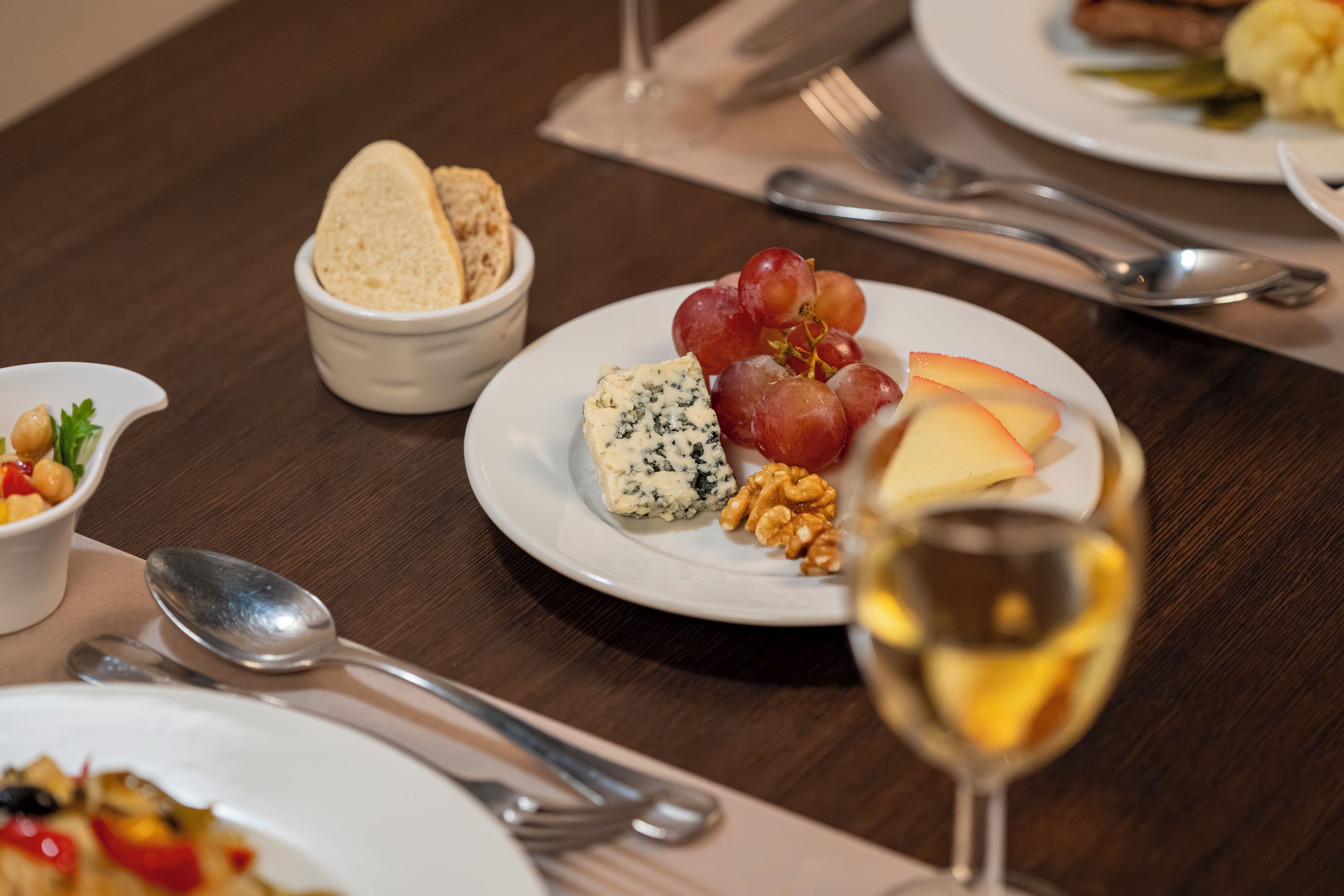 A dining table with plates of food, cutlery, and a glass of wine.