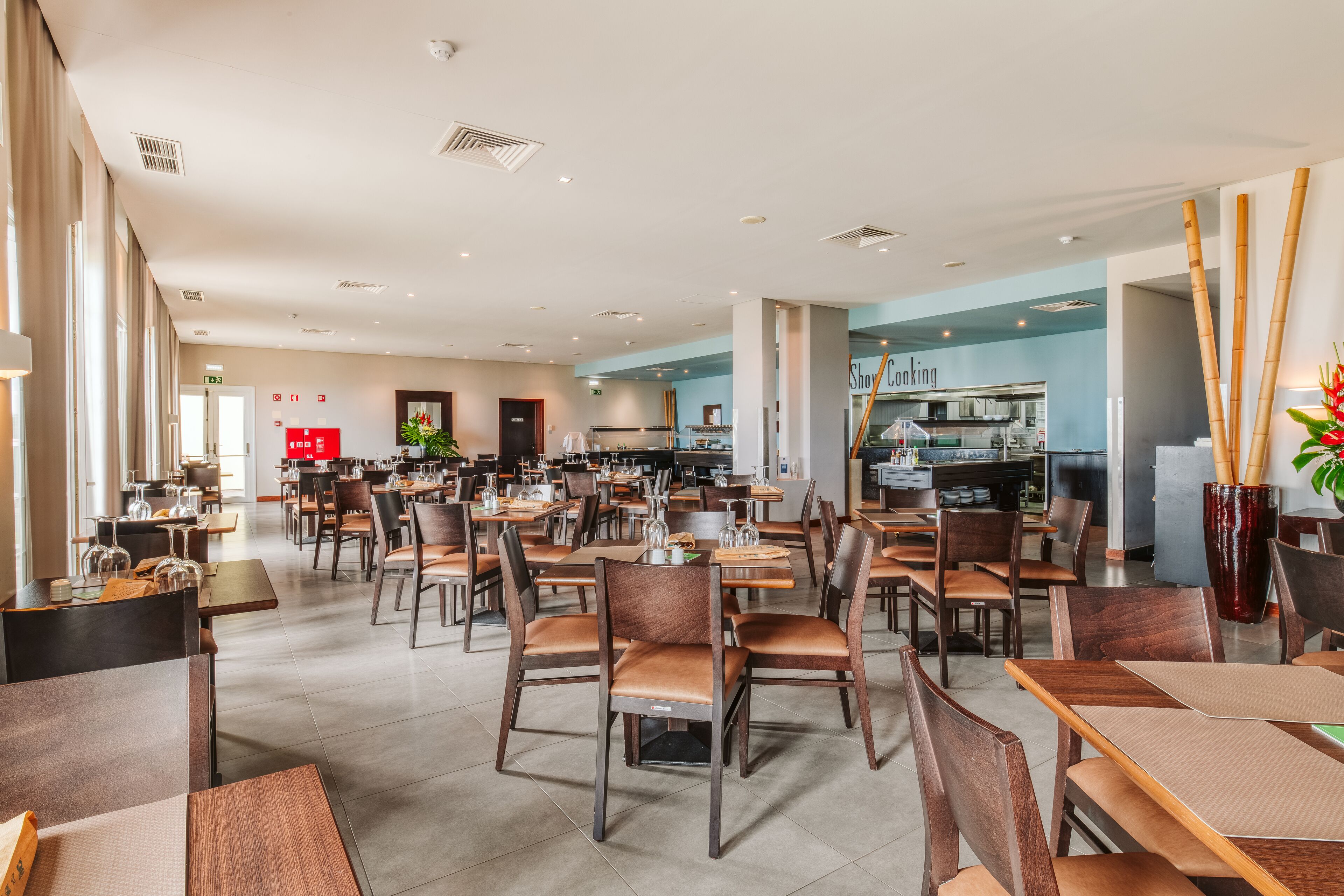 A spacious dining area with multiple tables and chairs, a kitchen in the background, and a modern interior design.