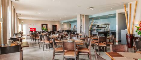 A spacious dining area with multiple tables and chairs, a kitchen in the background, and a modern interior design.
