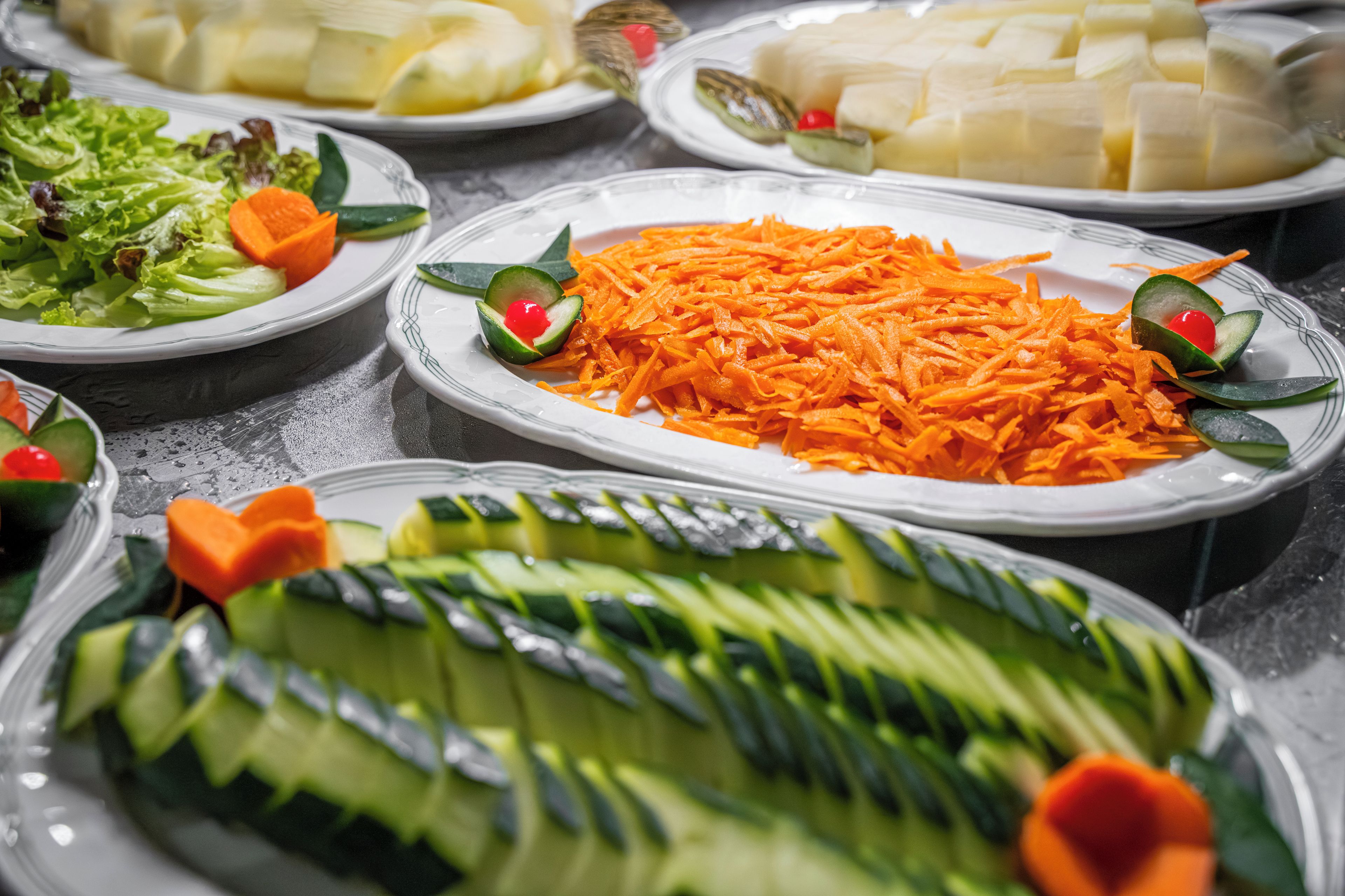Ein reichhaltiges Buffet mit verschiedenen Speisen, darunter Gurkenscheiben, geriebene Karotten und Blattsalat.