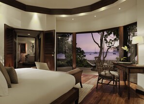 A bedroom with a large bed, a desk, and a view of the sea.