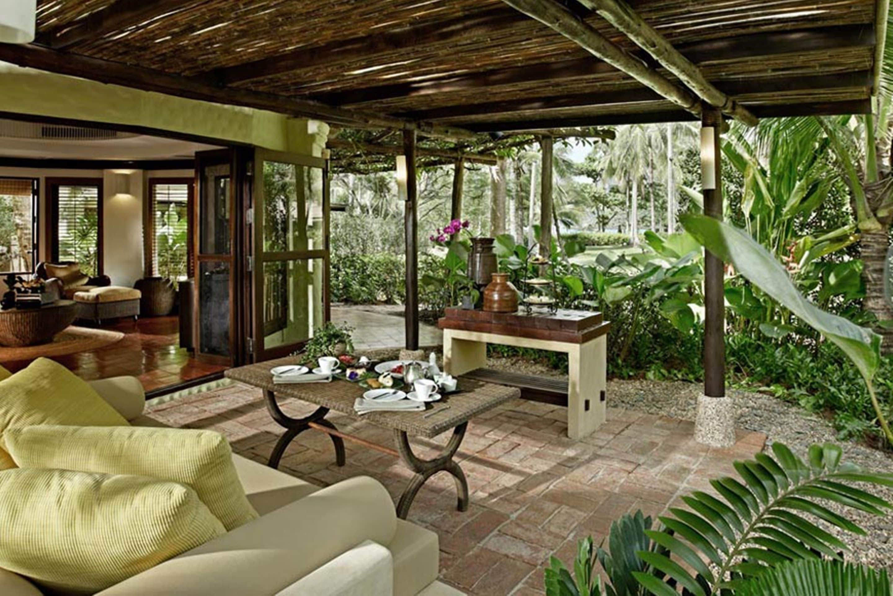 Ein überdachter Außenbereich mit Tisch für zwei Personen, umgeben von üppiger tropischer Vegetation und einer Holzpergola.