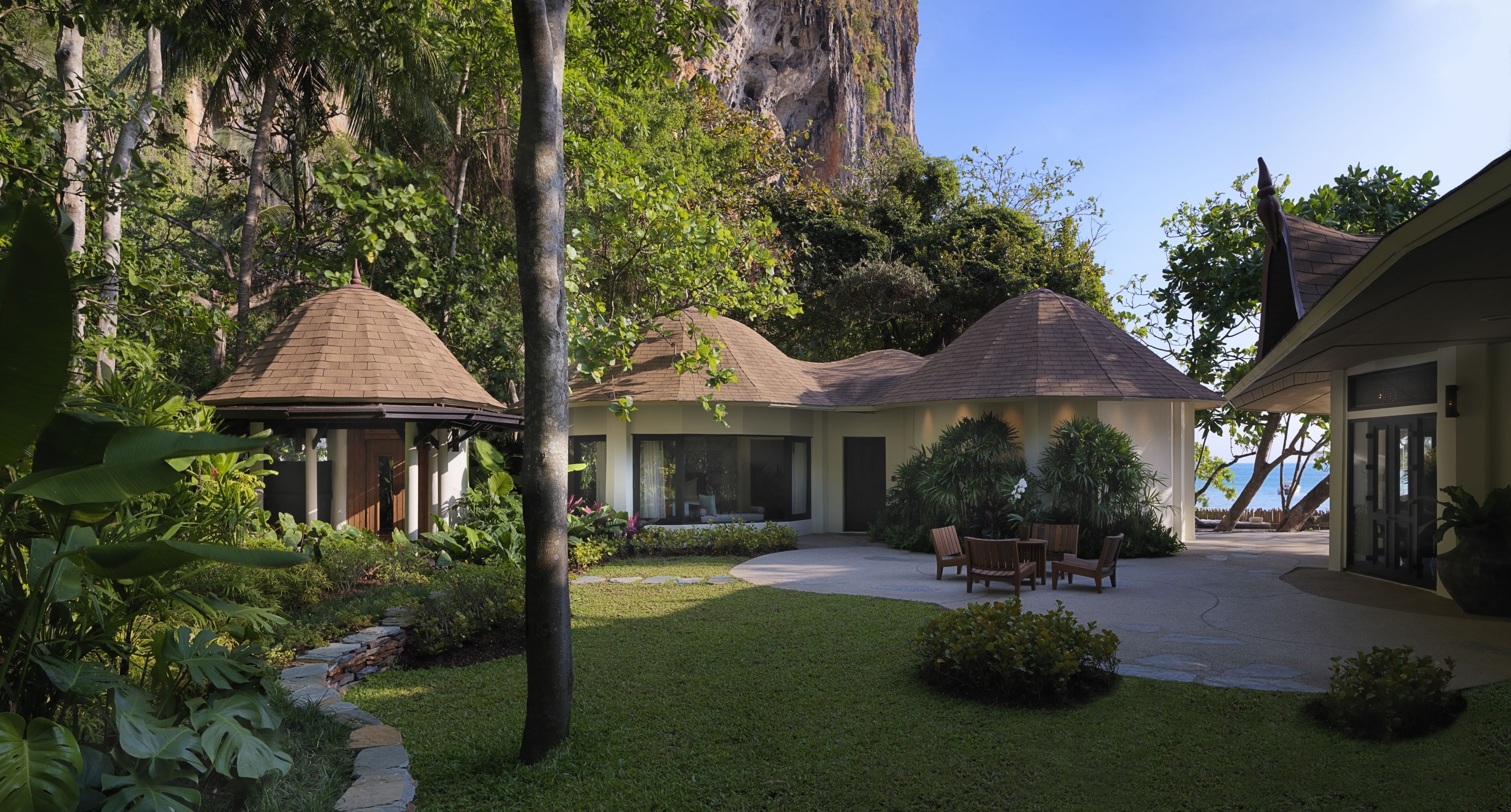 A modern house with a patio, surrounded by lush greenery and a large rock formation.