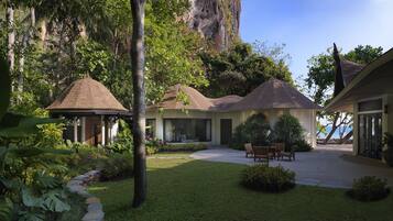 A modern house with a patio, surrounded by lush greenery and a large rock formation.