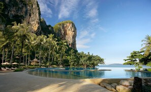 A resort with a pool, palm trees, and a cliff.