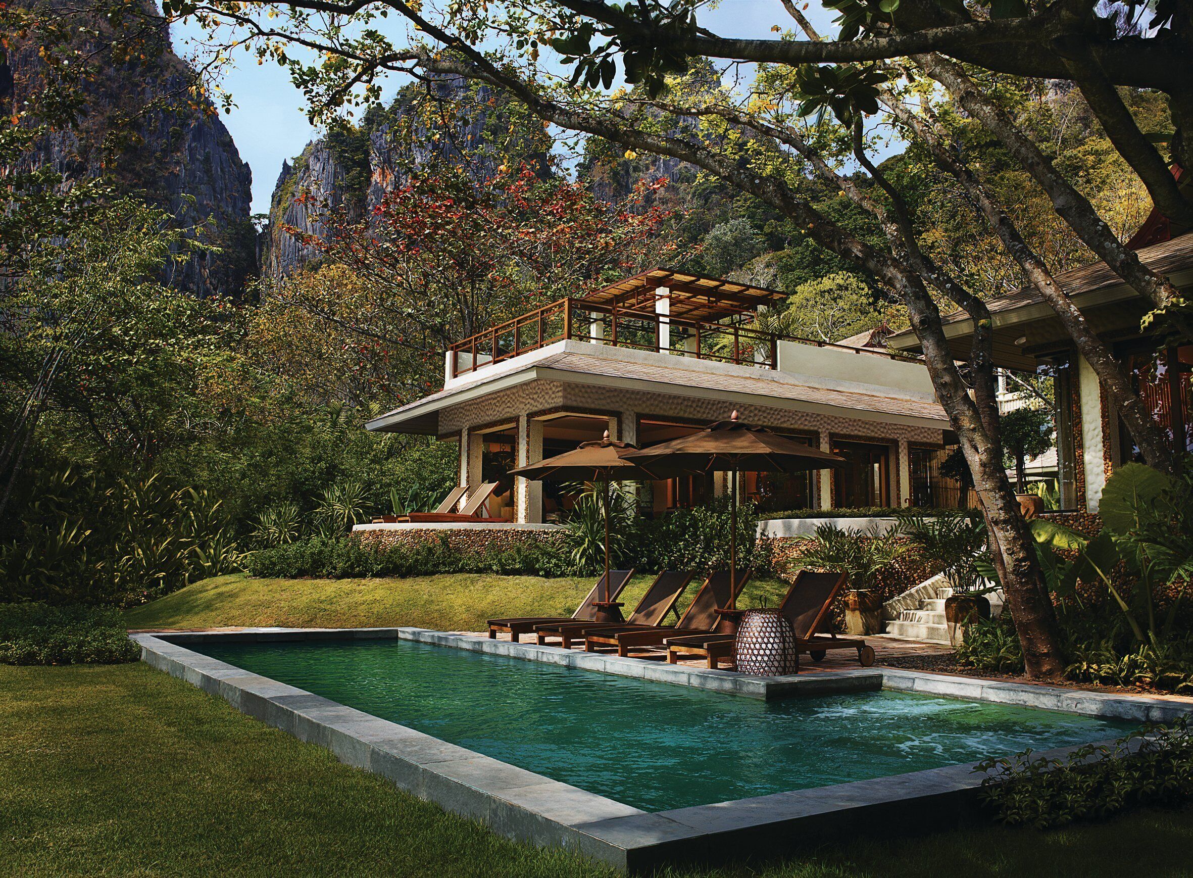 A modern house with a pool, surrounded by lush greenery and mountains.