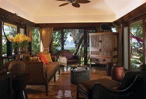 A spacious living room with a view of the sea, furnished with a sofa, chairs, and a wooden cabinet.