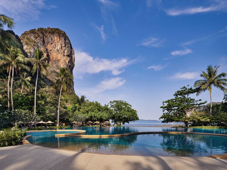 Zwembad van een resort met uitzicht op een klif en palmbomen.