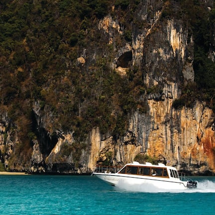 A boat on a turquoise sea with a rocky cliff in the background.