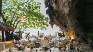 An outdoor dining area with round tables set for a meal, surrounded by natural rock formations and trees. - Rayavadee (Krabi)