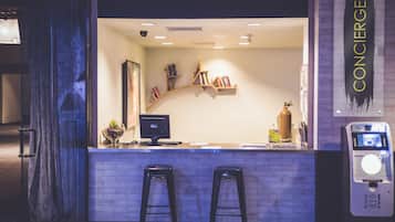 A modern bar area with a counter, two stools, a computer monitor, bookshelves, and a payment machine.