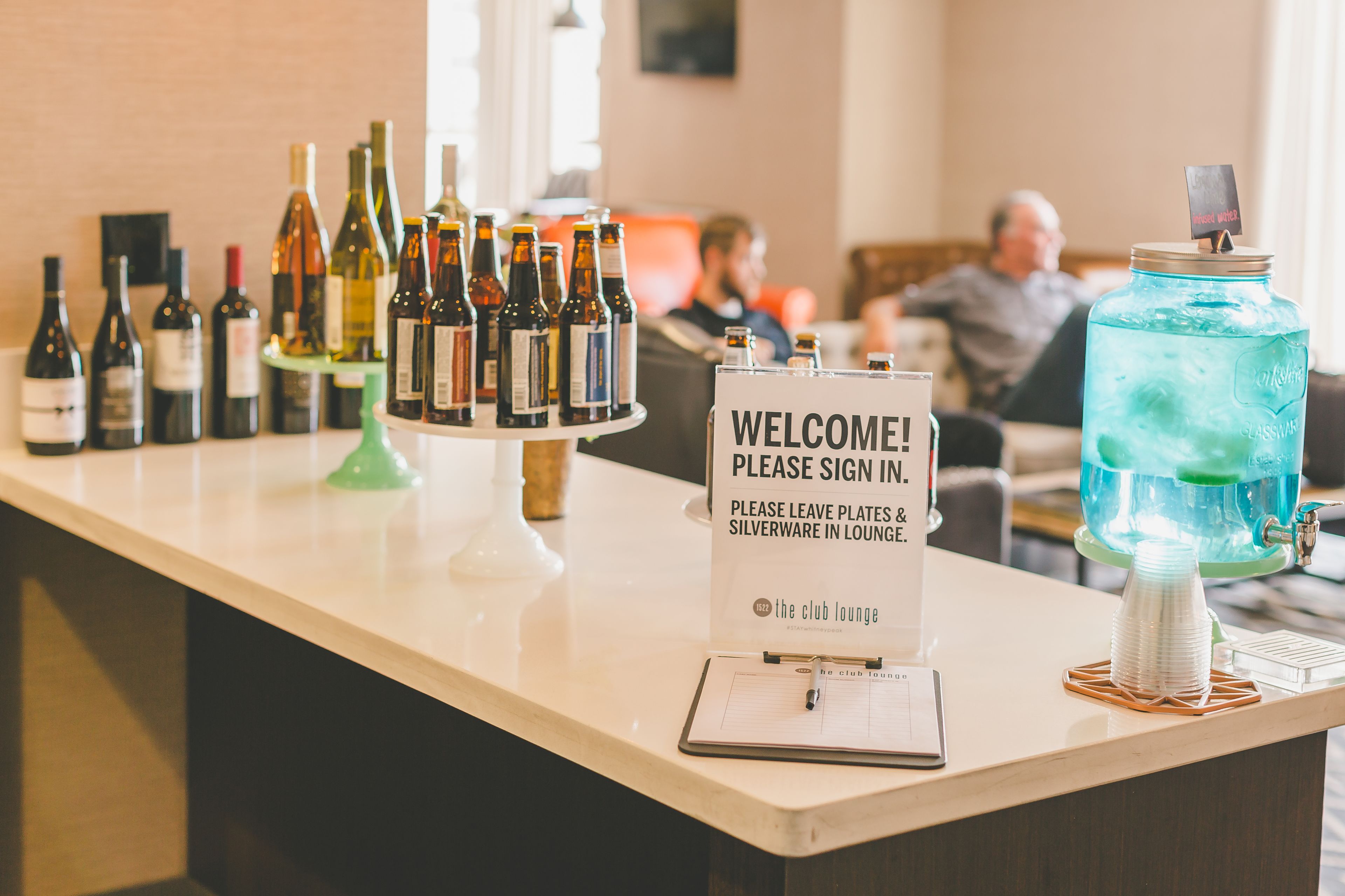 A reception area with a sign for the club lounge, a variety of wine bottles, and a water dispenser.