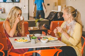 Two people dining at a table with various dishes, including scrambled eggs and a salad, in a modern dining area with orange chairs and a white table. - Whitney Peak Hotel Reno, Tapestry Collection by Hilton (Reno)
