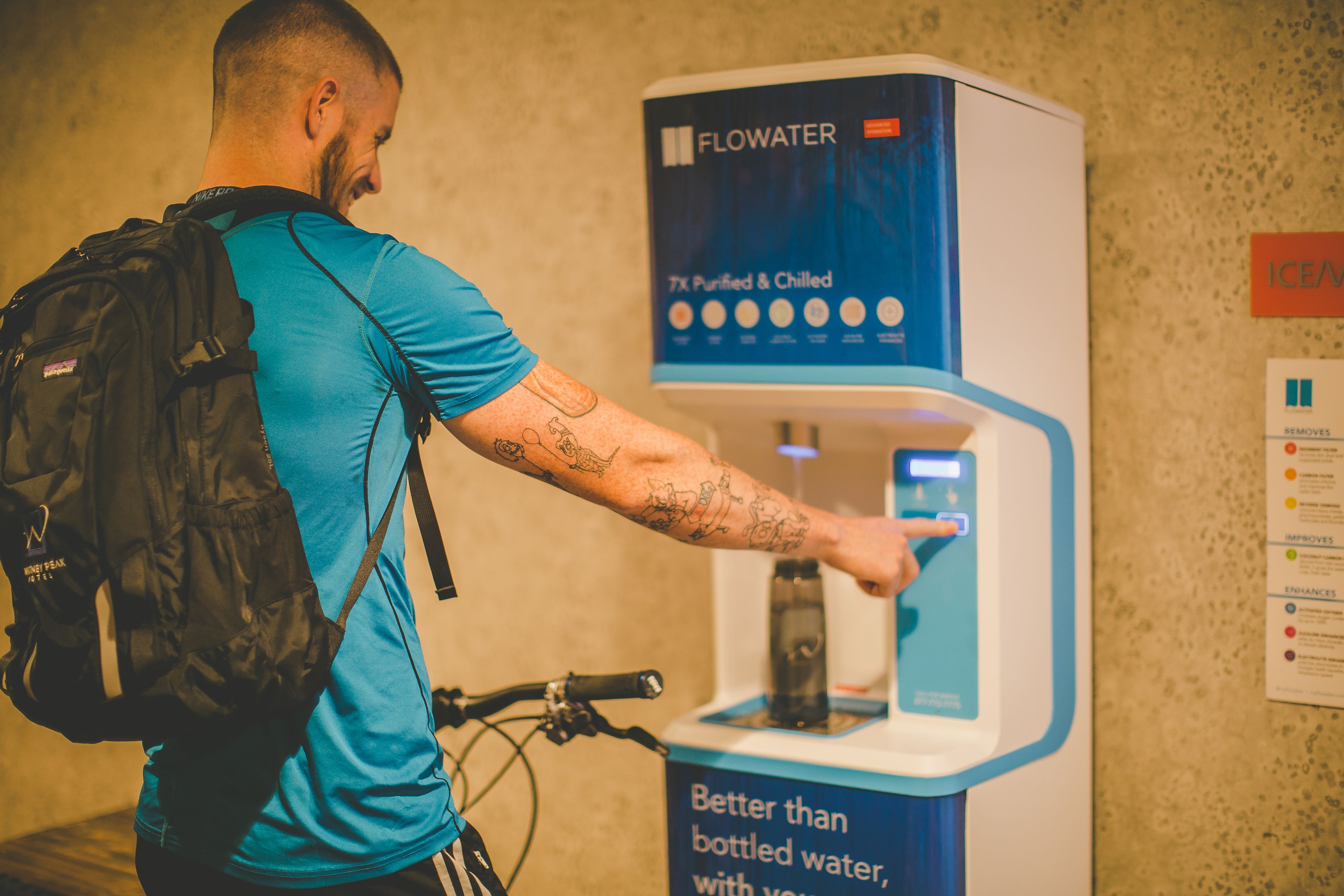 A person using a water dispenser with a sign stating "Better than bottled water, with your water."