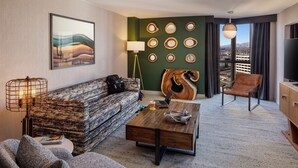 Una habitación de hotel moderna con sofá, sillón, mesa de centro y un ventanal con vistas a la ciudad.