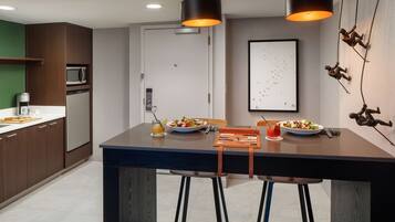 Una cocina moderna con encimeras oscuras, una isla central con taburetes, un microondas y un refrigerador.